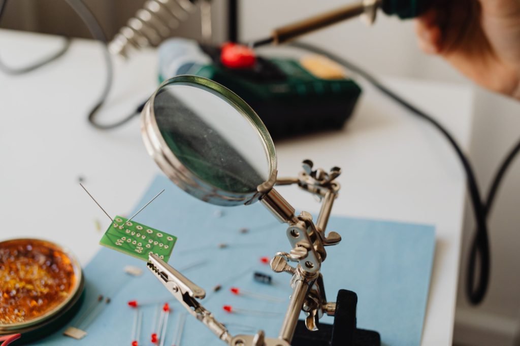 A circuit board being inspected under a magnifying glass at a bench