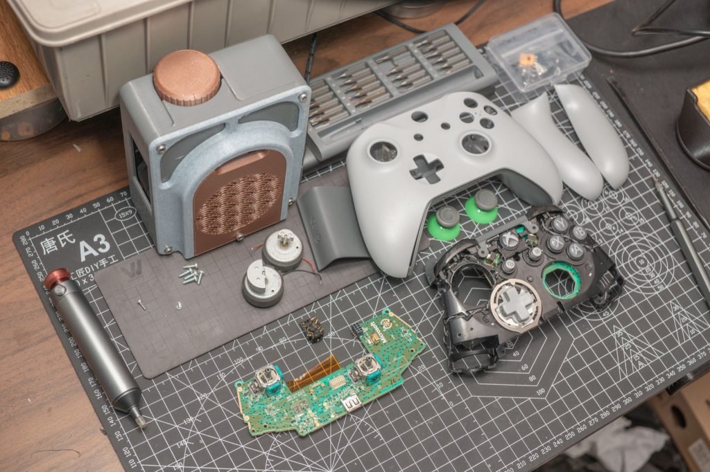 Disassembled game controller with its circuit board and parts laid out on a bench mat