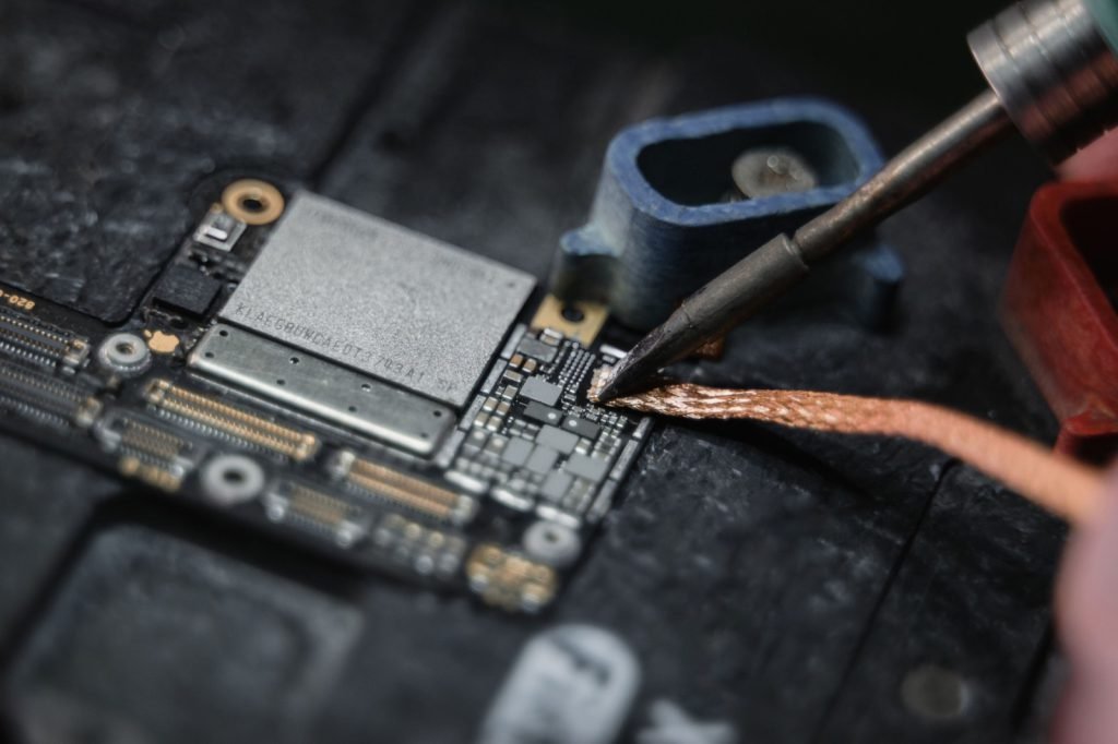 A soldering iron working on a densely populated circuit board at a repair bench