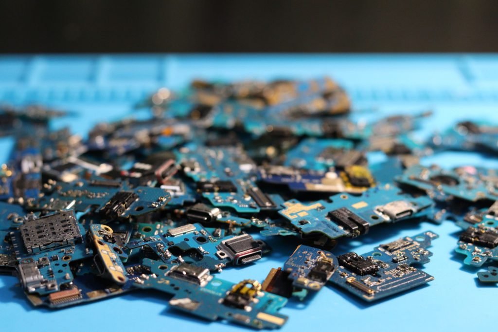 A heap of small disassembled circuit boards and components on a workbench mat