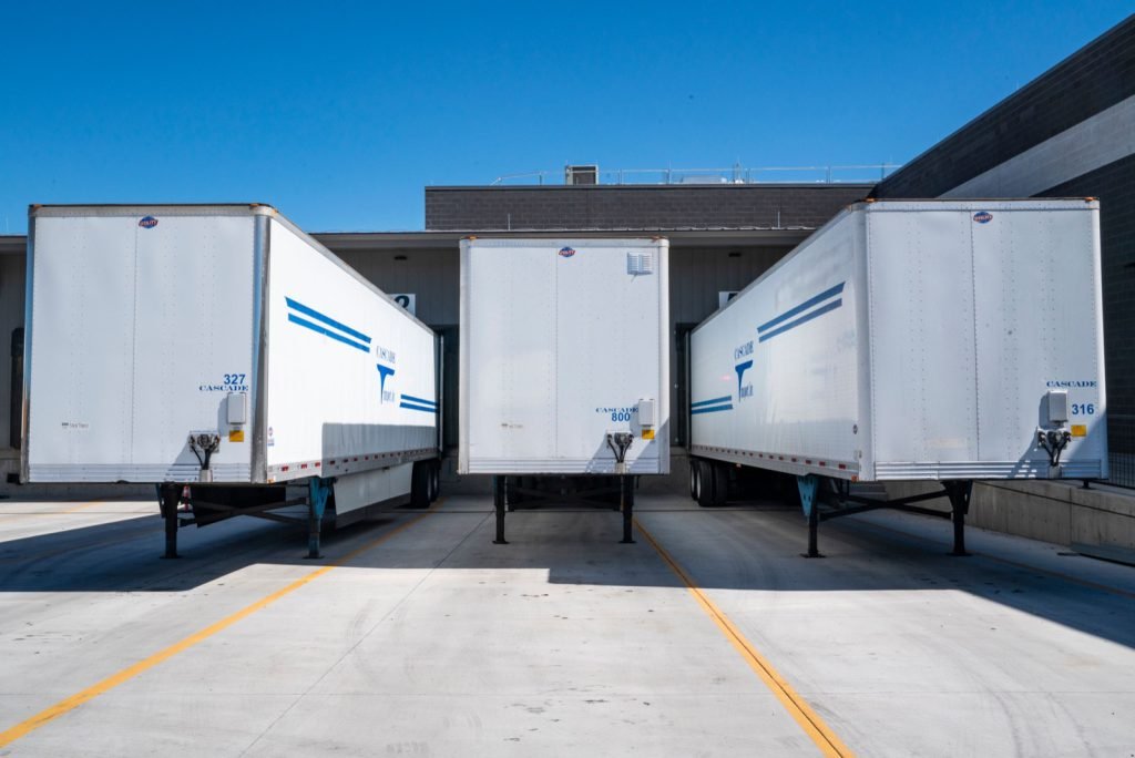 Three enclosed freight trailers backed into loading dock doors