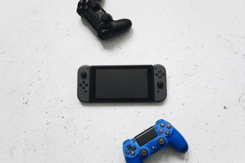 A Nintendo Switch laid out between PlayStation controllers on a pale surface
