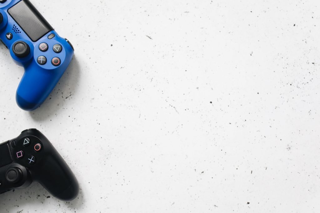 A blue and a black PlayStation controller on a pale surface