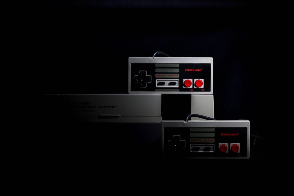 A retro games console and two controllers lit against a dark background