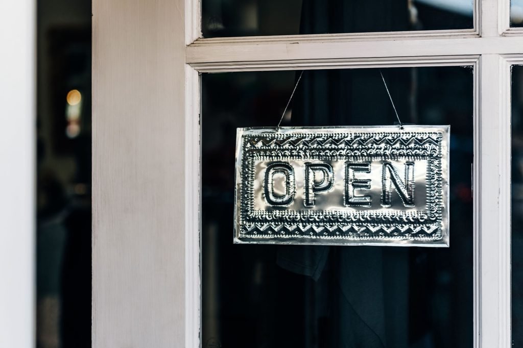 A metal open sign hanging on the glass door of an independent shop