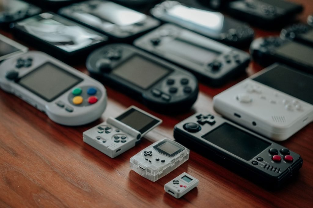 A row of assorted handheld game consoles laid out across a wooden counter