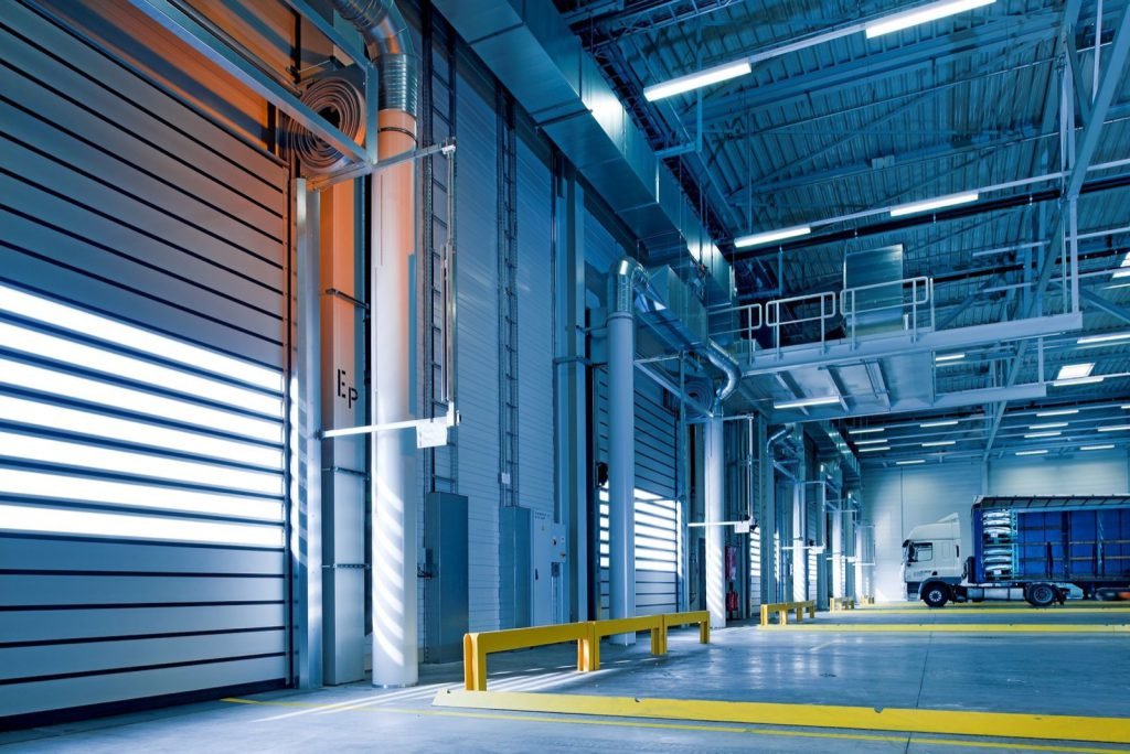 A truck standing inside a warehouse dock bay beside roller shutter doors