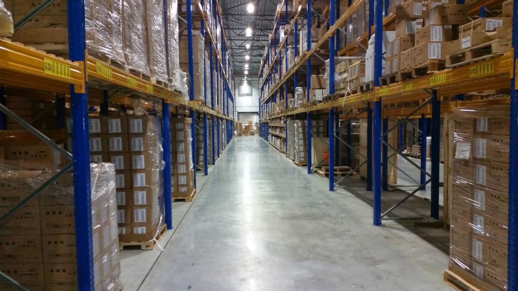 A long warehouse aisle lined with racked and shrink-wrapped pallets