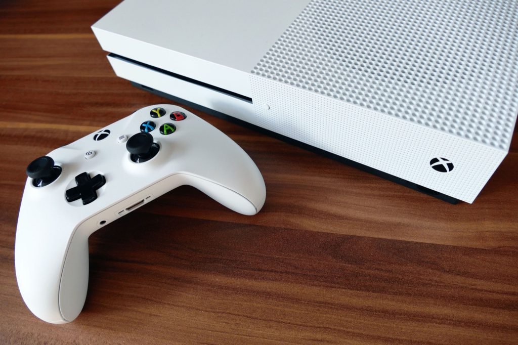 A white Xbox One S console beside its controller on a wooden surface