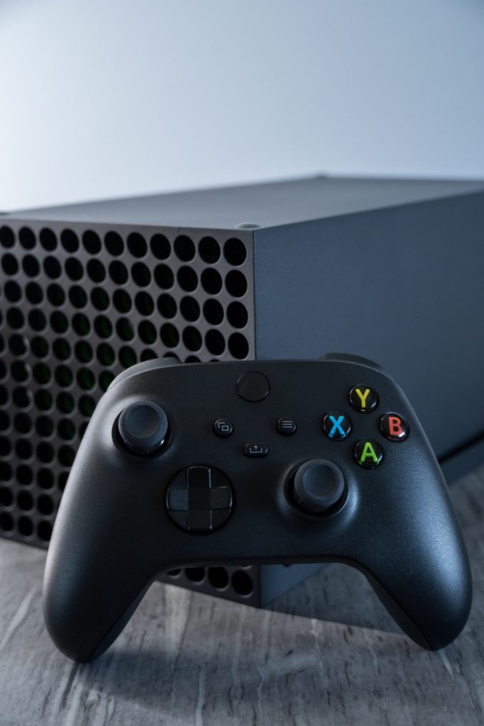An Xbox Series X console standing behind its black wireless controller